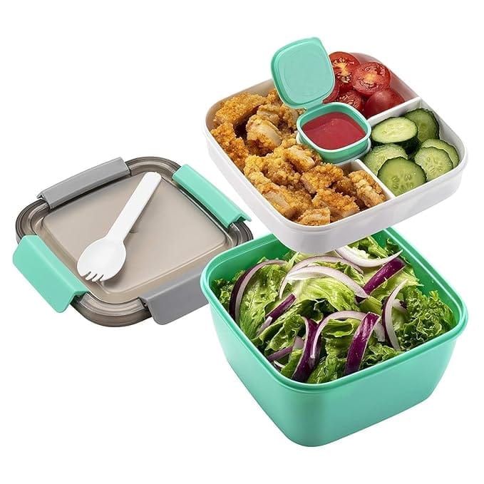The image shows a plastic food container with a salad, chicken, and vegetables. The container is divided into three compartments, and it has a lid with a spoon. The product title could be "Three Compartment Lunch Container with Lid and Spoon".